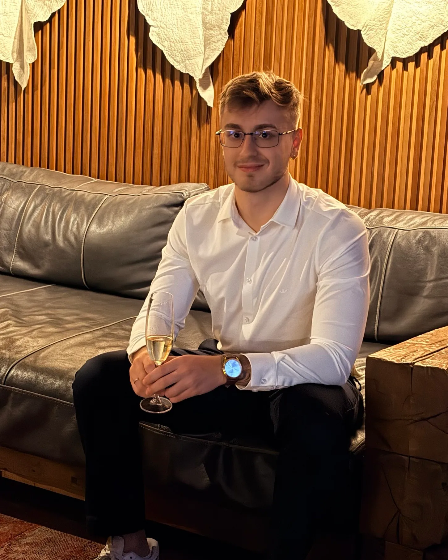 Motter, founder of Studio Tenna, sitting on a leather sofa in a white shirt, smiling at the camera